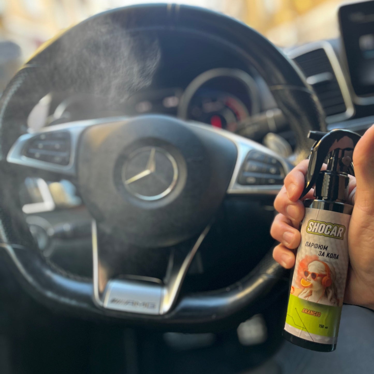 Person using a SHOCAR air freshener spray in a car with a visible steering wheel.