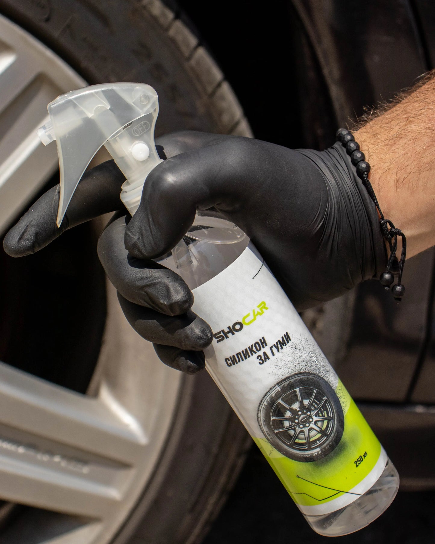 Person applying a tire cleaning product to a car tire with a spray bottle.
