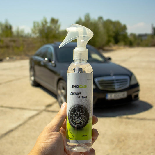 Бутилка SHOCAR силикон за гуми, държана на открито пред черен луксозен автомобил – продукт за поддръжка и блясък на автомобилни гуми.