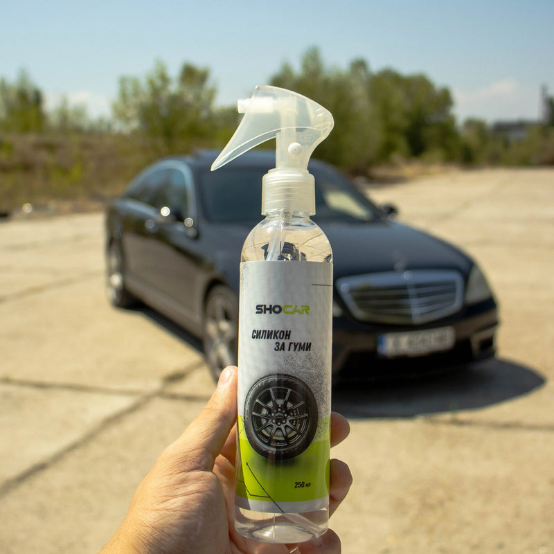Бутилка SHOCAR силикон за гуми, държана на открито пред черен луксозен автомобил – продукт за поддръжка и блясък на автомобилни гуми.